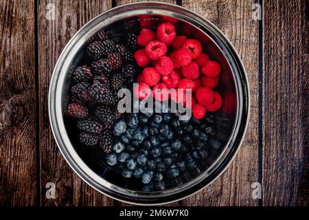 Heidelbeeren, Himbeeren und Brombeeren in einer Mischschüssel: Eine Mischung aus drei Arten frischer Beeren in einer großen Metallschüssel Stockfoto