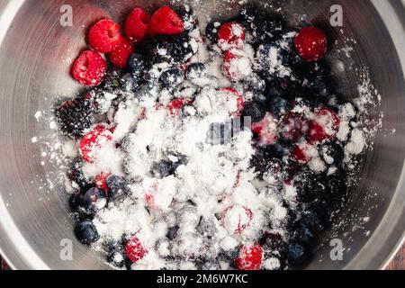 Gemischte Beeren mit Maisstärke, Zucker und Zitronensaft: Zutaten in Kuchenfüllung in eine Mischschüssel voller frischer Beeren gegeben Stockfoto