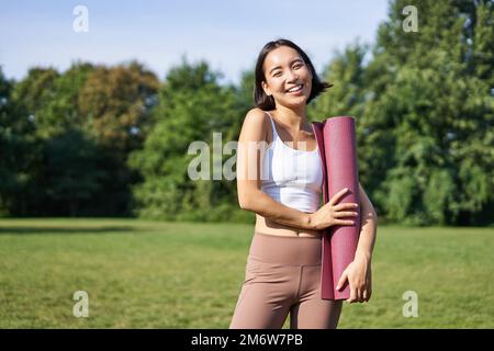 Porträt eines asiatischen Mädchens lächelt und lacht, steht mit Sportausrüstung, Gummimatte, trägt Uniform für Workout und Übungen in p Stockfoto