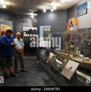 Gary Royse (rechts), Freiwilliger Dozent im Hampton Roads Naval Museum, stellt am Freitag, den 6. Mai 2022, Fragen von einem Besucher seiner Galerie. Das Museum befindet sich im zweiten Stock des Nauticus Campus in Downtown Norfolk, Virginia, und beherbergt ein robustes Freiwilligenkorps, das Besuchern hilft, die Geschichte der Marine in der Gegend um Hampton Roads, Virginia, kennenzulernen. Stockfoto