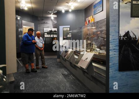 Gary Royse (rechts), Freiwilliger Dozent im Hampton Roads Naval Museum, stellt am Freitag, den 6. Mai 2022, Fragen von einem Besucher seiner Galerie. Das Museum befindet sich im zweiten Stock des Nauticus Campus in Downtown Norfolk, Virginia, und beherbergt ein robustes Freiwilligenkorps, das Besuchern hilft, die Geschichte der Marine in der Gegend um Hampton Roads, Virginia, kennenzulernen. Stockfoto