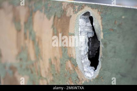 Krieg in der Ukraine, ein Loch in der Rüstung der BMP, durchbohrte Rüstung. Textur von grünem getarntem gepanzertem Metall mit Schäden und Löchern. Stockfoto