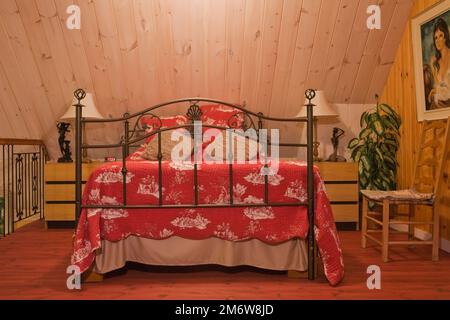 Queen-Size-Himmelbett mit schmiedeeisernem Kopfteil und Fußbrett im Hauptschlafzimmer im Obergeschoss im Blockhaus. Stockfoto