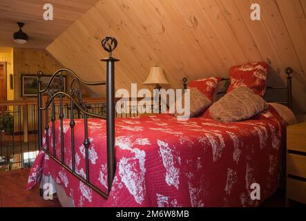 Queen-Size-Himmelbett mit schmiedeeisernem Kopfteil und Fußbrett im Hauptschlafzimmer im Obergeschoss im Blockhaus. Stockfoto