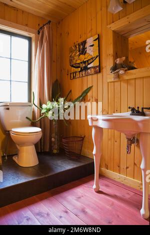 Antikes Waschbecken und Toilette aus weißem Porzellan auf erhöhter Plattform im Gästebad auf Zwischengeschoss im Blockhaus. Stockfoto