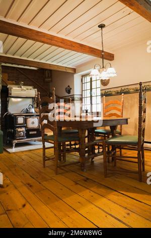 Antiker Holztisch und Stühle mit hoher Rückenlehne, 1850er Jahre Sweet Heart Retro-Kochherd handgefertigt von Elmira Herd arbeitet in der Küche im Blockhaus. Stockfoto