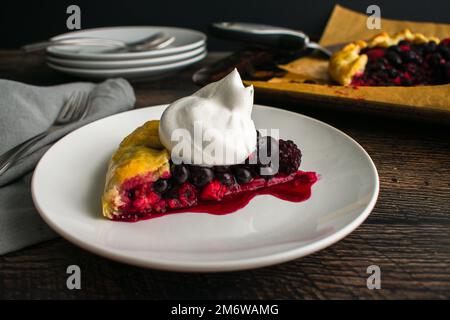 Scheibe gemischte Beerengalette garniert mit Schlagsahne: Rustikale Dessertttorte mit Himbeeren, Heidelbeeren und Brombeeren Stockfoto