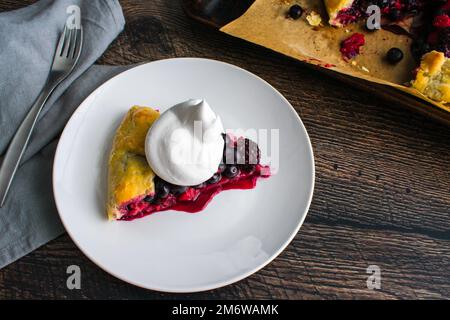 Scheibe gemischte Beerengalette garniert mit Schlagsahne: Rustikale Dessertttorte mit Himbeeren, Heidelbeeren und Brombeeren Stockfoto