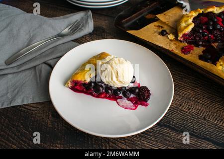 Ein Stück gemischte Beerengalette garniert mit Vanilleis: Rustikale Dessertttorte mit Himbeeren, Heidelbeeren und Brombeeren Stockfoto