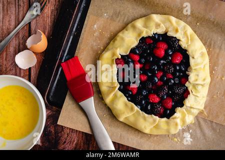 Unaked Mixed Berry Galette on a Perchment-Lined Sheet Pan: Rustikale Desserttart mit Himbeeren, Heidelbeeren und Brombeeren Stockfoto