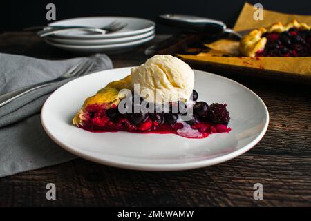 Ein Stück gemischte Beerengalette garniert mit Vanilleis: Rustikale Dessertttorte mit Himbeeren, Heidelbeeren und Brombeeren Stockfoto