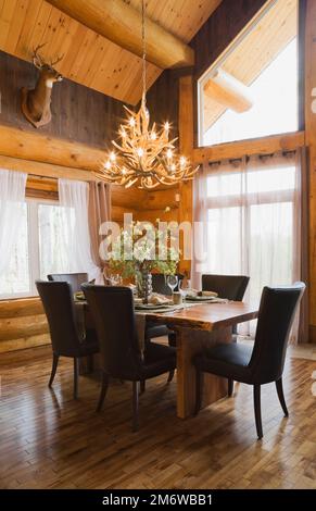 Esstisch aus Naturholz und braune Lederstühle im Esszimmer im luxuriösen Blockhaus im Cottage-Stil. Stockfoto