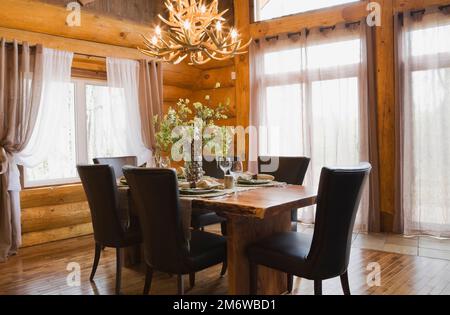 Esstisch aus Naturholz und braune Lederstühle im Esszimmer im luxuriösen Blockhaus im Cottage-Stil. Stockfoto