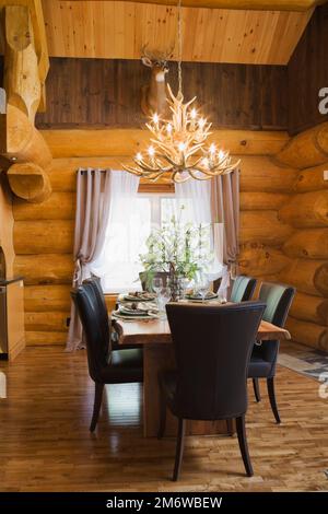 Esstisch aus Naturholz und braune Lederstühle im Esszimmer im luxuriösen Blockhaus im Cottage-Stil. Stockfoto