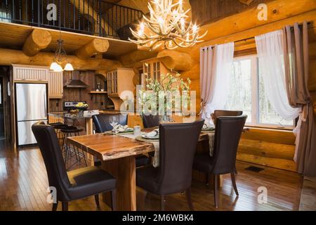 Esstisch aus natürlichem Holz und braune Lederstühle im Esszimmer plus Küche mit Quarz-Ablageflächen und Insel im luxuriösen Blockhaus. Stockfoto