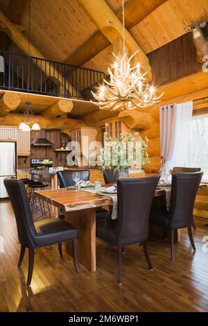 Esstisch aus natürlichem Holz und braune Lederstühle im Esszimmer plus Küche mit Quarz-Ablageflächen und Insel im luxuriösen Blockhaus. Stockfoto