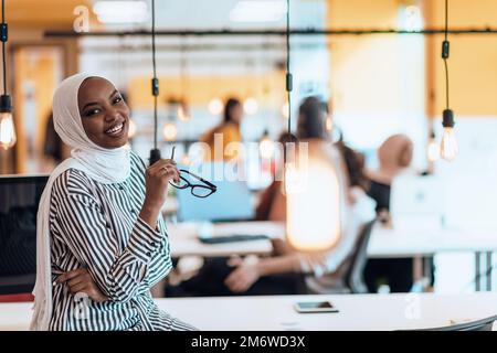 Trait einer schwarzen (afroamerikanischen) weiblichen muslimin, die in einem modernen Geschäftsbüro steht, während sie einen Hijab trägt. Stockfoto