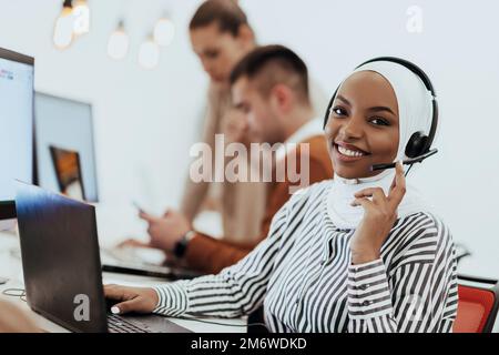 Afroamerikanische muslimische Frau mit Hijab und Headset, die als Kundensupport in einem modernen Büro arbeitet. Stockfoto
