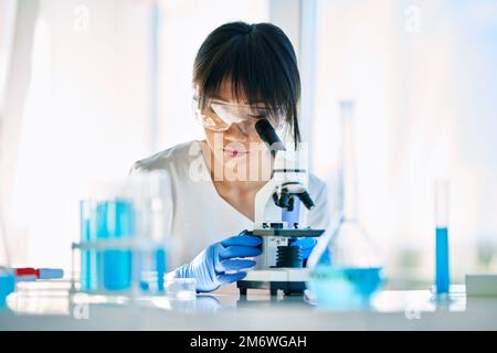 Porträt eines asiatischen Wissenschaftlers, der durch ein Mikroskop an der medizinischen Forschung im modernen Labor schaut Stockfoto