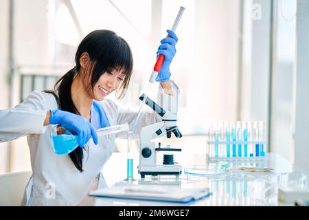 Ein glücklicher, lächelnder Wissenschaftler, der Forschung macht und Reagenzien in Reagenzgläser gießt Stockfoto