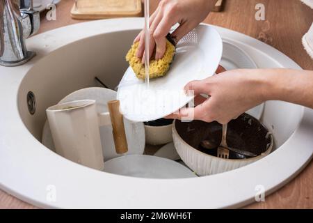 Frauenhände waschen den Teller unter fließendem Wasser. Dreckiges Geschirr im Waschbecken in der Küche, Chaos Stockfoto