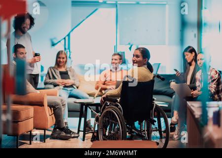 Geschäftsfrau im Rollstuhl, die ein Geschäftstreffen mit dem Team in einem modernen Büro führt. Eine Gruppe junger Freiberufler vereinbart online neue Stockfoto