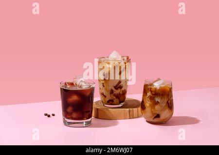 Eiskaffee in einem großen Glas mit Sahne und Kaffeebohnen. Set mit verschiedenen Arten von Kaffeegetränken auf einem rosafarbenen Tisch. Stockfoto