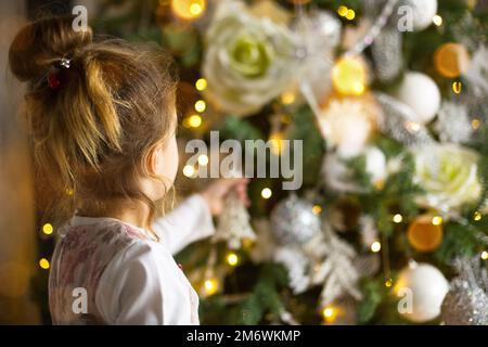 Ein kleines Mädchen greift mit der Hand nach einem Weihnachtsbaumspielzeug. Weihnachtsdekor, wartet auf einen Feiertag Stockfoto