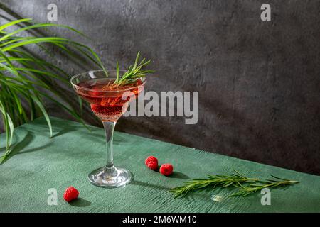 Sommerlicher erfrischender alkoholischer Cocktail. Himbeerlimonade mit frischem Rosmarin garniert. Sommergetränk mit Himbeeren und Sekt Stockfoto