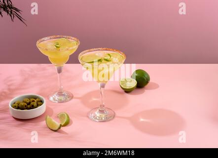 Margarita-Cocktail. Konzept klassischer Getränke. Erfrischende, farbenfrohe Sommergetränke auf pinkfarbenem Hintergrund mit Palmenblättern. Bar Stockfoto