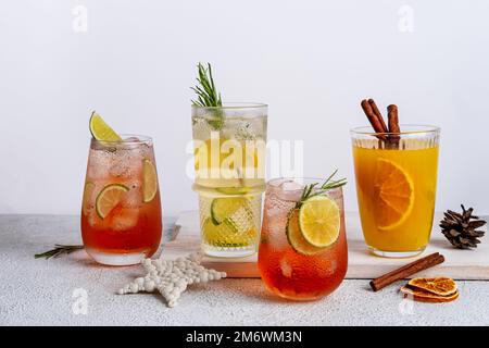 Vier farbenfrohe Weihnachtscocktails in Gläsern auf einem weißen Tisch. Auswahl an frischen Urlaubsgetränken. Erdbeermojito, Orangenpunsch Stockfoto