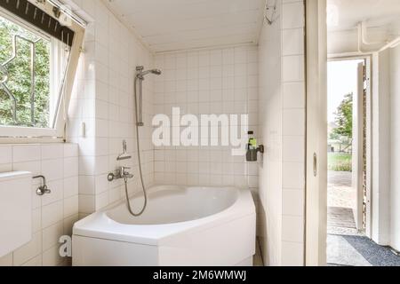 Ein kleines Bad mit Toilette und Waschbecken in der Ecke, neben einem offenen Fenster mit Blick auf Bäume Stockfoto