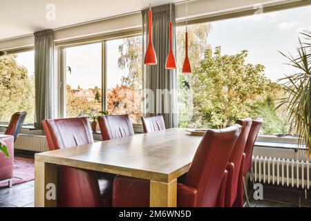 Ein Speisesaal mit roten Stühlen und einem Holztisch vor großen Fenstern mit Blick auf die Bäume draußen Stockfoto