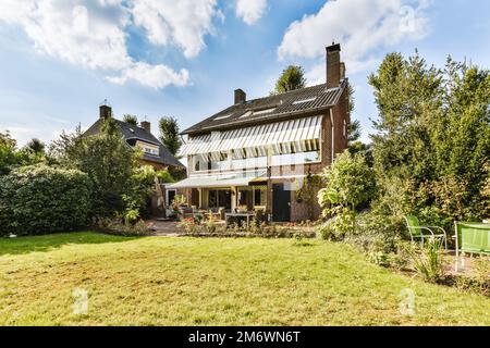 Ein Haus, das sich in der Mitte einer Gegend mit grünem Gras und Bäumen auf beiden Seiten des Hauses befindet Stockfoto