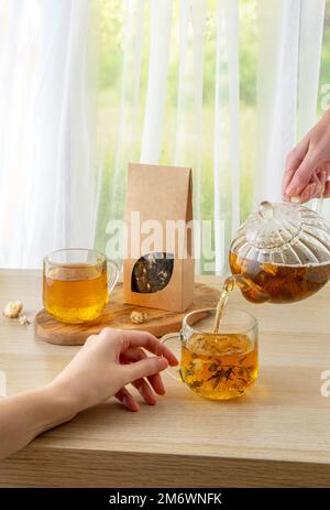 Bio-Teemarkierung und Verpackungsmodell. Grüner Jasmintee in Glas Teekanne auf dem Tisch. Heißer Tee ist in den Glasbechern. Teekanne und Stockfoto