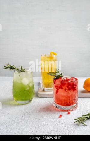 Drei farbenfrohe Sommercocktails in Gläsern auf einem weißen Tisch. Auswahl an frischen Sommergetränken. Rote Sangria-Cocktails, Orangenpunsch Stockfoto