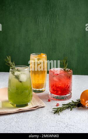 Drei farbenfrohe Sommercocktails in Gläsern auf einem grauen Tisch. Auswahl an frischen Sommergetränken. Rote Sangria-Cocktails, Orangenpunsch Stockfoto