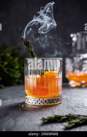 Negroni mit rauchendem Rosmarin. Negroni mit Eis und Orange auf dunklem Hintergrund. Negroni-Cocktail in einem Glas mit rauchendem Rosema Stockfoto