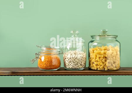 Verschiedene Hülsenfrüchte in Glasgefäßen: Pasta, Bohnen, Linsen auf grünem Hintergrund. Keine Abfalllagerung, plastikfrei. Stockfoto