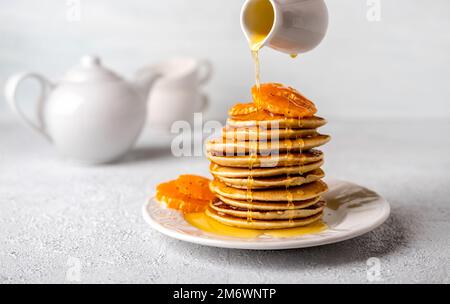 Leckere Pfannkuchen mit Honig oder Ahornsirup zum Frühstück auf hellem Hintergrund aus nächster Nähe. Stockfoto