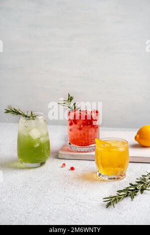 Drei farbenfrohe Sommercocktails in Gläsern auf einem weißen Tisch. Auswahl an frischen Sommergetränken. Rote Sangria-Cocktails, Orangenpunsch Stockfoto