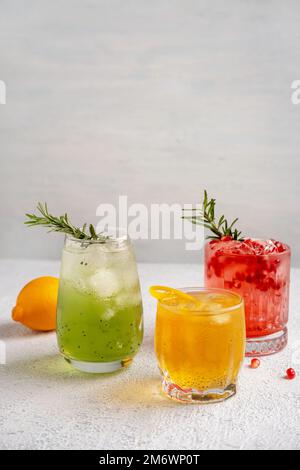 Drei farbenfrohe Sommercocktails in Gläsern auf einem weißen Tisch. Auswahl an frischen Sommergetränken. Rote Sangria-Cocktails, Orangenpunsch Stockfoto