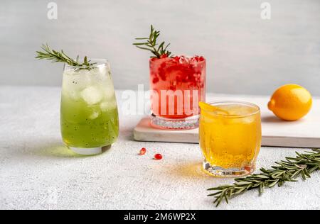 Drei farbenfrohe Sommercocktails in Gläsern auf einem weißen Tisch. Auswahl an frischen Sommergetränken. Rote Sangria-Cocktails, Orangenpunsch Stockfoto