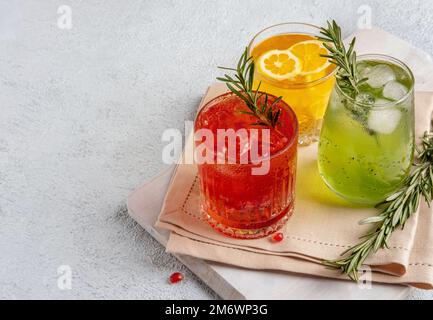 Drei farbenfrohe Sommercocktails in Gläsern auf einem weißen Tisch. Auswahl an frischen Sommergetränken. Rote Sangria-Cocktails, Orangenpunsch Stockfoto