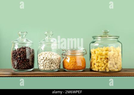 Verschiedene Hülsenfrüchte in Glasgefäßen: Kichererbsen, Pasta, Bohnen, Erbsen, Linsen auf grünem Hintergrund. Keine Abfalllagerung, plastikfrei. Stockfoto