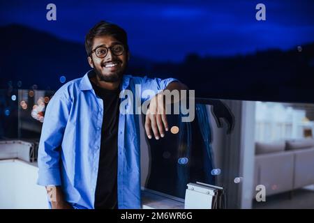 Ein Inder mit Brille und blauem Hemd schaut nachts um die Stadt. Im Hintergrund der Nachtstraße der Stadt Stockfoto