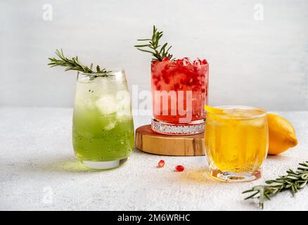 Drei farbenfrohe Sommercocktails in Gläsern auf einem weißen Tisch. Auswahl an frischen Sommergetränken. Rote Sangria-Cocktails, orangefarbenes pu Stockfoto