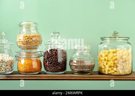 Verschiedene Hülsenfrüchte in Glasgefäßen: Kichererbsen, Pasta, Bohnen, Erbsen, Linsen auf grünem Hintergrund. Keine Abfalllagerung, plastikfrei. Stockfoto