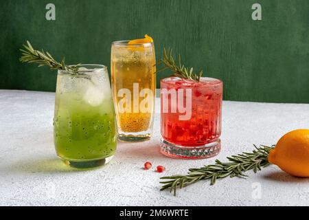 Drei farbenfrohe Sommercocktails in Gläsern auf einem grauen Tisch. Auswahl an frischen Sommergetränken. Rote Sangria-Cocktails, orangefarbenes Wortspiel Stockfoto
