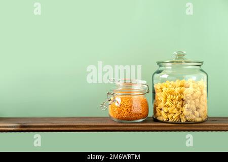 Linsen und Pasta in Glasgefäßen auf grünem Hintergrund. Keine Abfalllagerung, plastikfrei. Stockfoto